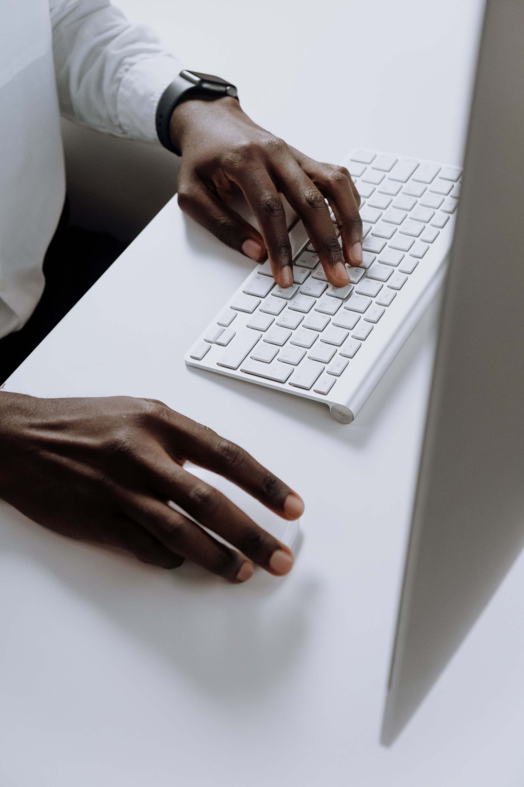 Hands typing on a keyboard at a desk with monitors nearby, hands typing on a sleek keyboard in an office setting